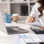 Charming Young asian businesswoman sitting on laptop computer in the office, asian employee business making report calculating balance Internal Revenue Service checking document.