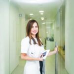 Smiling young female medical professional, doctor opening the door to her practice or hospital