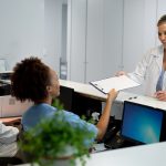 Caucasian female doctor passing document to african american receptionist at hospital reception