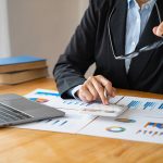 Businessperson analyzing charts with calculator and laptop