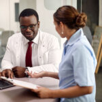 Happy African American doctor and nurse cooperating while using laptop at medical clinic.