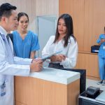 At hospital information counter doctor speaking to administrative crew checking patient status