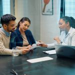 Black female financial advisor and couple going through savings plans in the office.