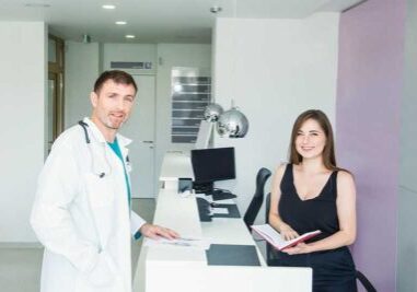 doctor standing at front desk of medical practice talking to receptionist