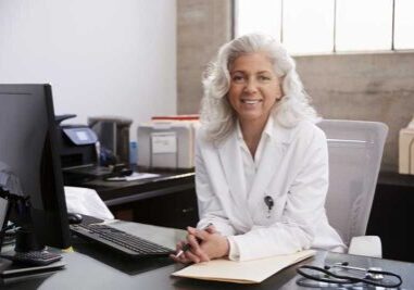 closeup of a female physician sitting at her desk with a computer, wireless keyboard and some paperwork