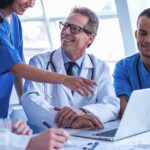 Successful medical doctors are using a laptop and smiling while having a discussion