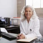closeup of a female physician sitting at her desk with a computer, wireless keyboard and some paperwork