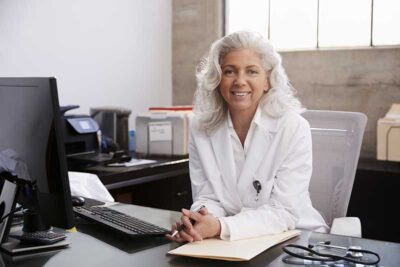 closeup of a female physician sitting at her desk with a computer, wireless keyboard and some paperwork